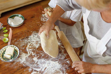 Frame picture of a female and kid hands holding dough in heart shape top view. Baking ingredients on the dark wooden table. Horizontal view.の写真素材