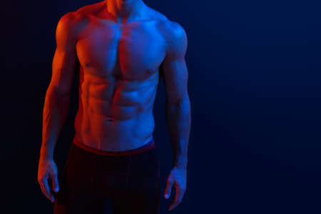 Cropped image of a strong athletic young man model showing six pack abs, over dark purple neon background.の写真素材