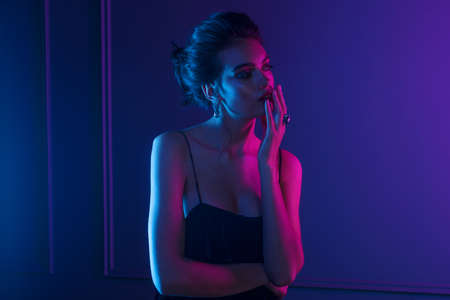 Sensual woman with bare shoulders, hairstyle and makeup, wear in elegant stone earrings, over dark purple neon lights. Studio shooting.の写真素材