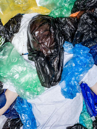 Top view of a young man with plastic bag on face, lying down, surrounded by plastic bags. Horizontal view.の写真素材