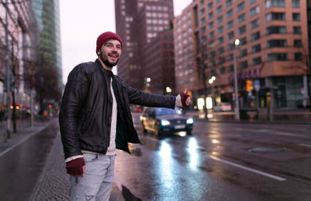 Young handsome happy hipster young man traveler hitchhiking along on road in the city.の写真素材
