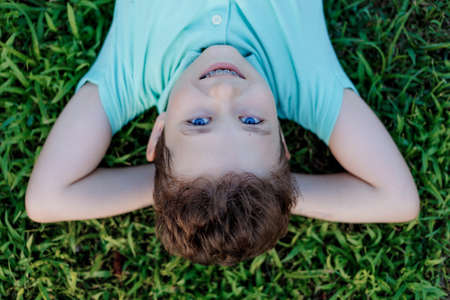 Portrait of cute smiling young boy with blue eyes and teeth braces lying on grass in park looking at camera.の写真素材