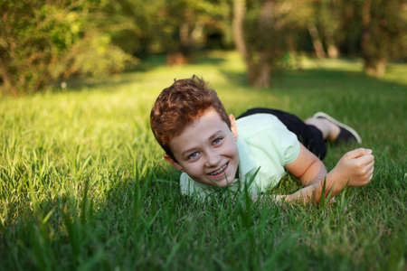 A smiling young boy lying on the grass, enjoys in the park, looks at the camera on a sunny summer day.の写真素材