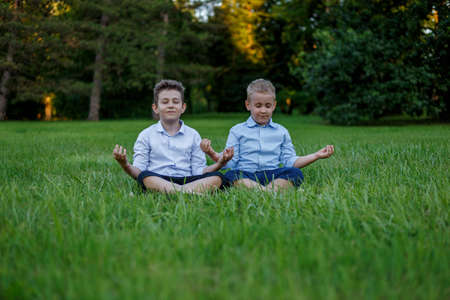 Two friends are meditating in the lotus position on a background of green meadows at the park.の写真素材