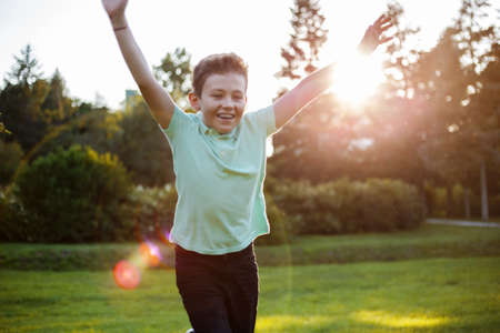 Happy boy runs with hands in the air, Child boy having fun playing outdoor activity, at the sunset background.の写真素材