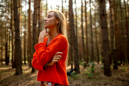 Portrait of a young woman dressed in an orange sweater in the fall park. Copy space.の写真素材