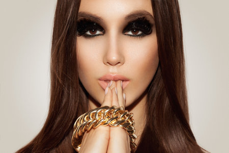Portrait of beautiful young woman with black smokey eyes,perfect tanned skin and gold jewelry in...