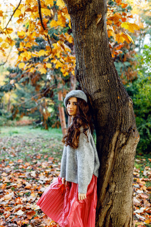 Attractive stylish girl with curly hair walking in park dressed in warm autumn trendy fashion, wearing beret hat.の写真素材