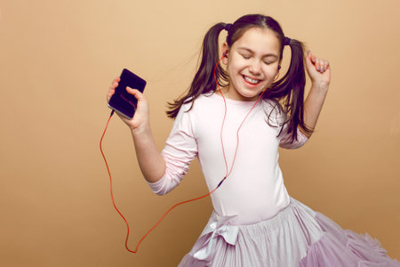 A pretty, little girl listening musin on her headphones, with closed eyes, posing in studio, on beige background.の写真素材