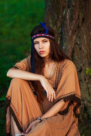 Front portrait of a attractive woman in native indian american boho dress sitting down on a grass in...