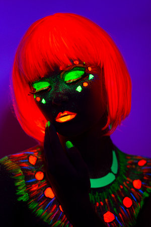 Front portrait of a female model with artistic neon colorful makeup and orange wig, isolated violet blue background.の写真素材