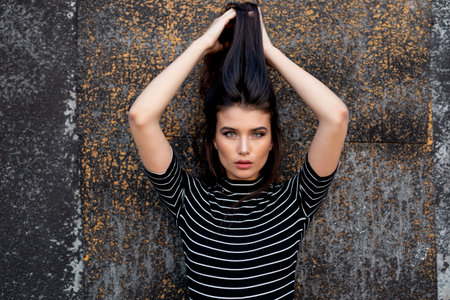 Sensual girl with straight brunette hair, makeup, supported by a black wall, looking at camera.の写真素材