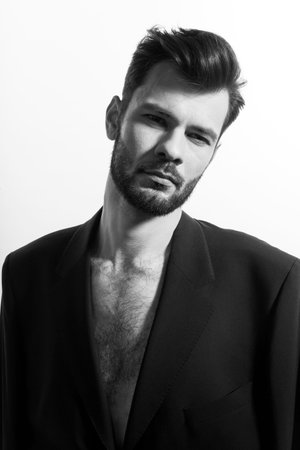 Handsome strong, brutal bearded man posing in black suit, with naked torso, isolated white background.の写真素材