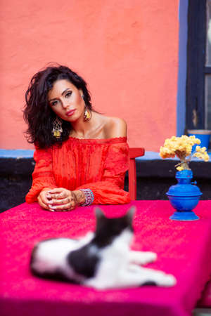 Beautiful young brunette woman with curly hair and makeup in sensual dress with bare shoulders,...