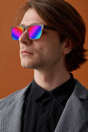 Front view shot of man, wearing grey clothes and sunglasses with multicolored lenses, on brown...