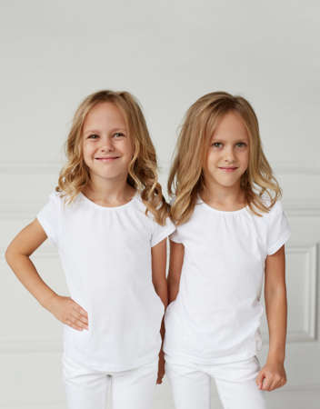 Two little smiling kids girls in white clothes isolated on white background. Twin girls they hold hands.の写真素材