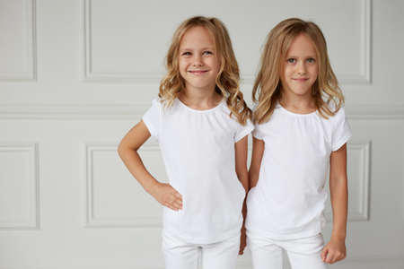 Two little smiling kids girls in white clothes isolated on white background. Twin girls they hold hands.の写真素材