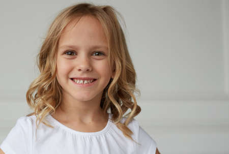 Portrait of a little girl smiling and looking at the camera, dressed in a white shirt, on a white background.の写真素材