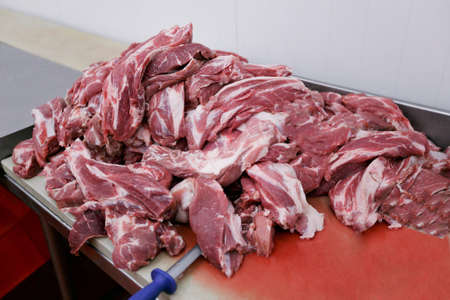 Closeup of a chopped a fresh meat in pieces on work table and knives in meat factory on industry of...