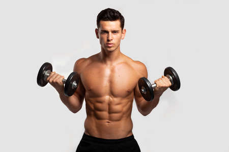 Front image of a confident young man with bare torso, training with dumb-bell, isolated white...
