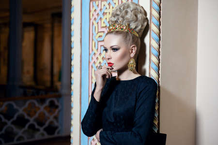 Young blonde female model, dressed in a long black dress with bow at the back, elegant hairstyle and crown and earrings.の写真素材