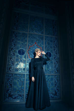 Full length image of a blonde model, dressed in a long black dress, with elegant hairstyle great crown and earrings.の写真素材