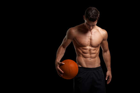 Portrait of a sexy handsome brunette young man with muscular body holding a bascket ball, posing at studio.の写真素材