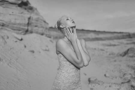 Closeup portrait. Profile portait of a blonde young woman in splendid slim gold dress posing in desert at the sunset.の写真素材