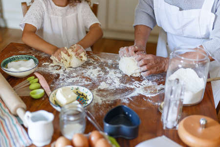 Frame picture of the hands of an senior woman and a child kneading dough. Ingredients for baking arranged on a table.の写真素材