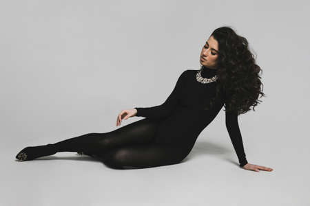 Full length image of a sexy young brunette curly woman in black bodysuit and high heel lies on the floor.の写真素材