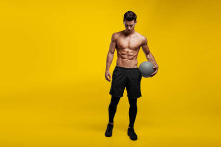 Full length of a handsome man with muscular body holding a basket ball, posing at studio, isolated yellow background.の写真素材