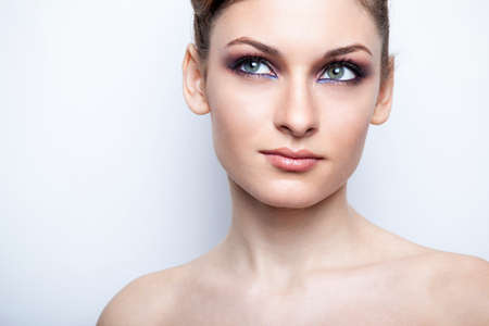 Front closeup portrait of a beautiful female model with bare shoulders with makeup, over light background.の写真素材