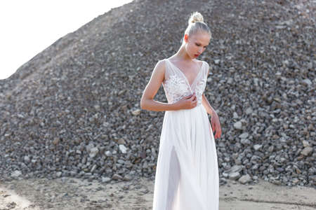 Blonde woman with hair tight up in white long bride dress, in day time, over piles of stones.の写真素材