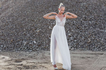 Full length view of a young woman in a white wedding dress, looking at camera, posed behind piles of stones.の写真素材