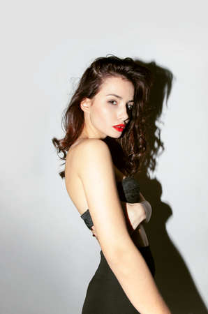 Attractive brunette young woman in black lengerie is possing sensual and looking at camera on grey...
