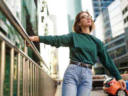 Portrait of a girl with short hairstyle, looking at the side posing on urban street, at modern buildings background.の写真素材