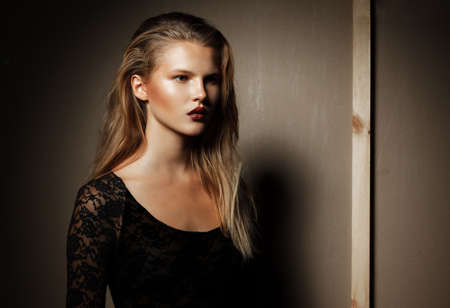 Stylish female model in black bodysuit with blonde hair, posing in the studio, looking at the side.の写真素材