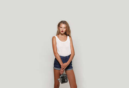 Attractive young blonde girl with make-up, holding in hands a retro camera, looking at camera.の写真素材