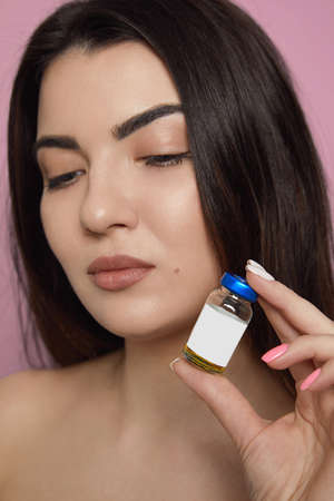 Closeup portrait of a beautiful young brunette woman with clean fresh skin on face, holding near...