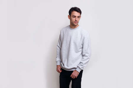 Frontal view of a handsome young brunette man in light gray jumper and black jeans over white background.の写真素材
