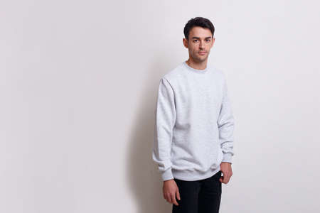 Frontal view of a smiling young brunette man in gray jumper and black jeans isolated white background.の写真素材