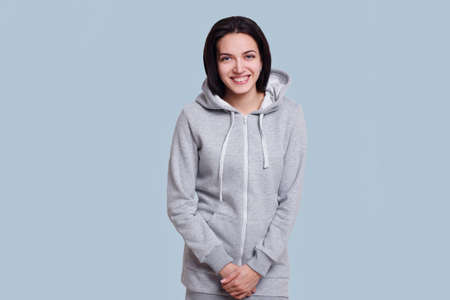Cheerful brunette model dressed in casual clothes shows smile and happy emotions isolated on light blue background.の写真素材