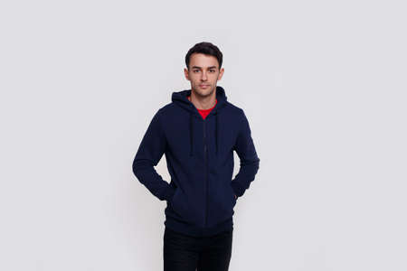 Frontal image of a smiling handsome young brunette man in dark blue jumper and jeans over white wall background.の写真素材