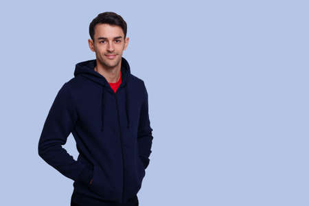 Frontal image of a smiling handsome young brunette man in dark blue jumper and jeans over blue background.の写真素材