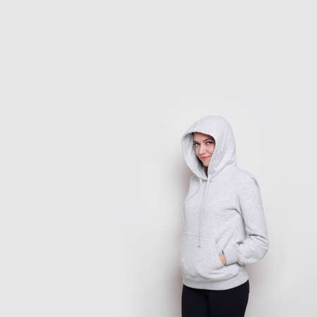Cherful brunette girl dressed in a light grey sweater with hood on her head, isolated on white background. Copy space.の写真素材