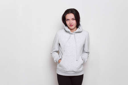 Young woman brunette dressed in a light grey sweater with hood on her head, isolated on white background. Space copy.の写真素材
