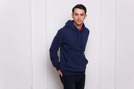 Handsome young man in dark blue jumper and jeans, holding his hands in his pockets, isolated white background. Horizontal view.の写真素材