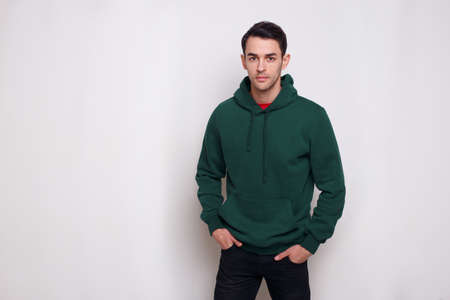Portrait of a confident young man in dark green jumper and jeans, with a hood on his head, isolated white background.の写真素材