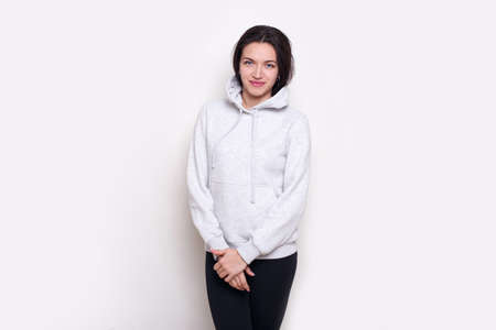 Young woman brunette in a light grey sweater, looking at camera, isolated on white background.の写真素材