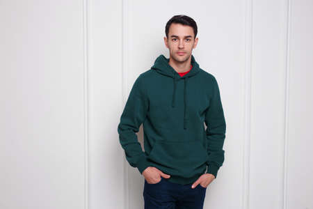 Portrait of a confident young man in dark green jumper and jeans, with a hood on his head, isolated white background.の写真素材